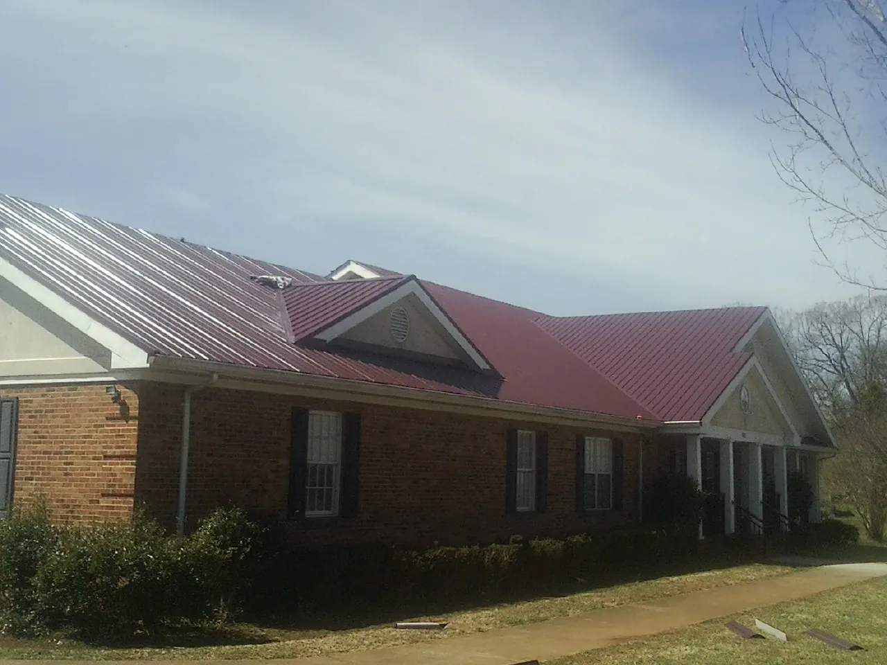 Red metal roof with gabled entries on a long brick building, from a Hail Damage Roof Repair job in Amite