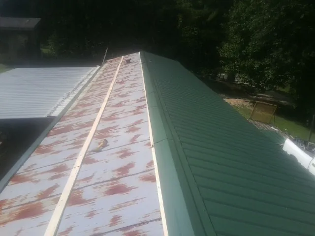 Old rusted panels beside newly installed green metal roofing — Wind Damage Roof Repair by Roofing Brothers in Amite