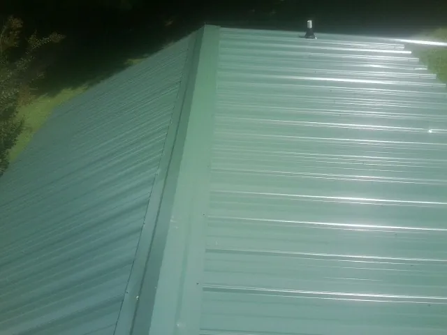 New green metal panels meeting at the ridge of a roof — Flat Roof Repair work by our crew in Amite