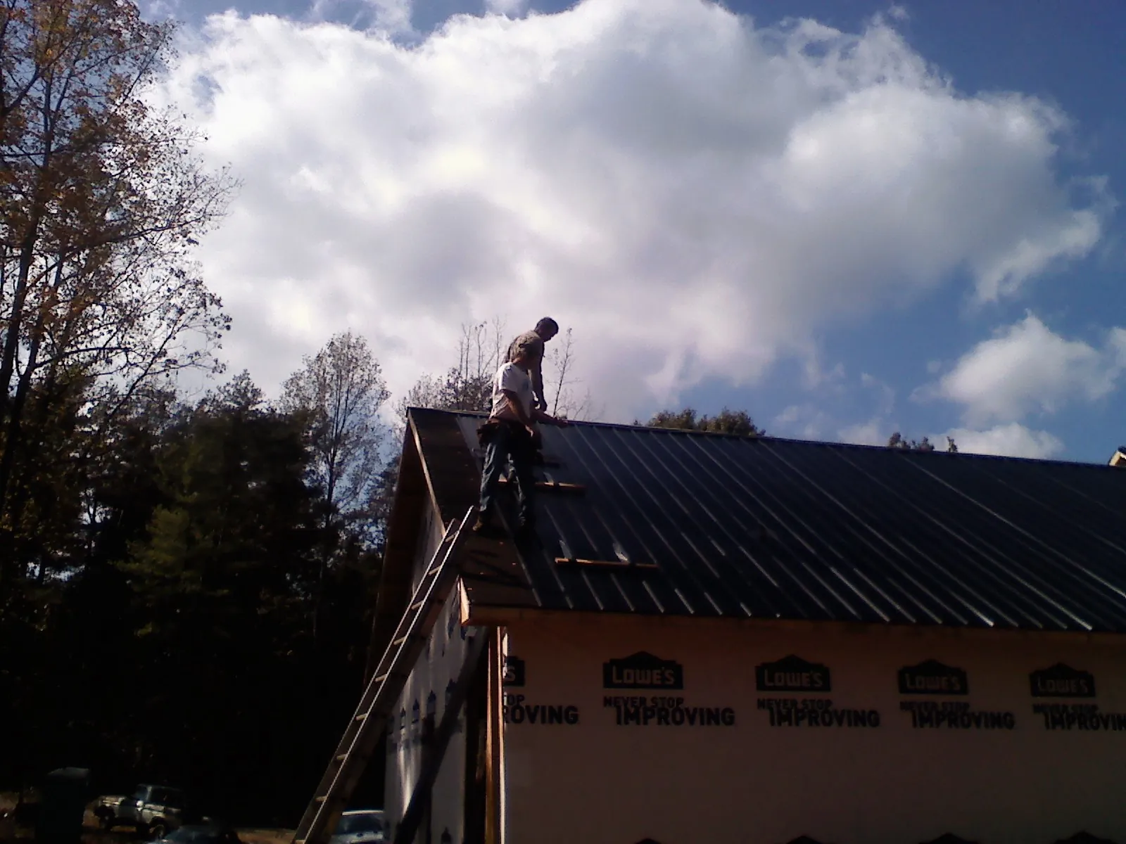 Roofer fastening dark metal panels high against a cloudy sky, from a Roof Inspection job in Amite